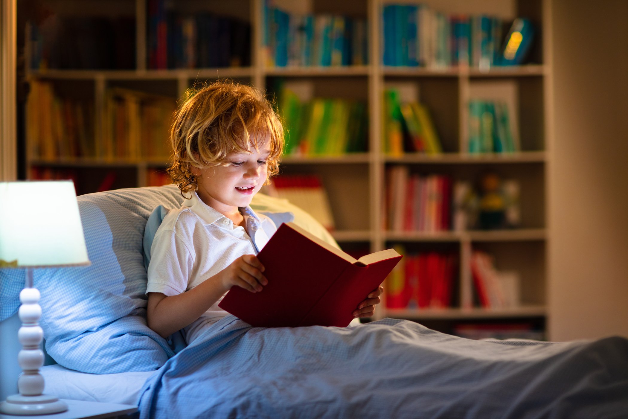 Child reading book in bed. Kids read at night.